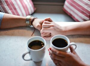 Pictured couple at the table with coffee cups, holding hands.