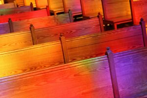 Quiet Impact of Churches blog post by Ken Walker Writer. Pictured: Empty church pews with light from stained glass windows shining on them.