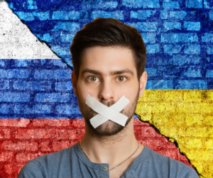 July 4 Marks the Freedom to Celebrate blog post by Ken Walker Writer. Pictured: A man with his mouth taped shut in front of a split wall painted with the Russian and Ukraine flags.