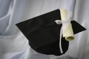 Graduating to New Dreams blog post by Ken Walker Writer. Pictured: A graduate cap and a diploma on a white fabric backdrop.