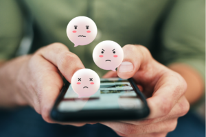 Voting One’s Conscience, Not Party blog post by Ken Walker Writer. Pictured: A man holding a phone and using social media with sad or angry emoticon bubbles coming out of it. as in fighting from the major political parties