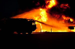 Comforting the Fire Victims blog post by Ken Walker Writer. Pictured: A fire truck backlit against raging wildfires.