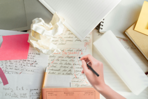 Pictured: A hand hovering over papers on a desk as if writing or editing them.