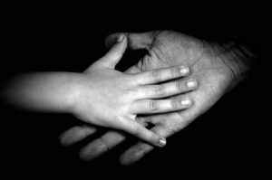A black and white photo zoomed in on a childs hand onto of their parents hand.