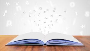 Leave Book Design to Graphic Artists blog post by Ken Walker Writer. Pictured: Letters flying onto the page of an open book.