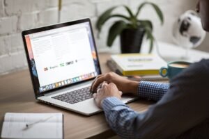 Pictured: A man using a laptop that is set on a desk. Only his arms can be seen.