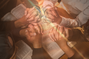 Pictured: A group of men's hands in prayer over open Bibles.