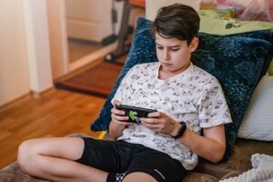 The Pandora’s Box of Technology blog post by Ken Walker Writer. Pictured: A boy lounging on aa couch with a device in his haands.