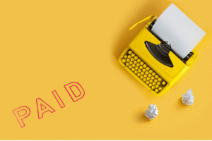 Writers Need a Tough Hide blog post by Ken Walker Writer. Pictured: A typewriter on a brilliant yellow background. A large paid stamp is off to the left. And a few crumpled balls of paper to the right.