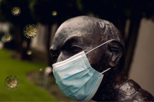 The Pandemic Scandals, Part 2 blog post by Ken Walker Writer. Pictured: A mask statue with covid like viruses hanging in the air around it.