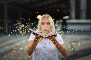 A joyful moment. Pictured: A women holds up a book as she blows colorful confetti at the camera.