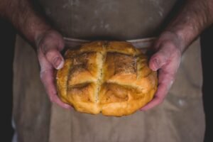 Good Writing Isn’t a 100-Yard Dash blog Post by Ken Walker Writer. Pictured: A baker in a flour dusted apron holding a golden loaf of bread.