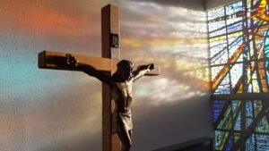 Good Friday Service. Pictured: A stain glass window shines on a sculpture of Jesus on the cross.