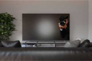 Pictured: A spy with a camera taking photos from a television set in a living room.