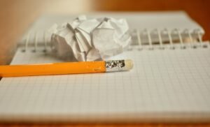 Write (or Edit) the Way You Should blog post by Ken Walker Writer. Pictured: An open notebook with a pencil and a crumpled up piece of paper resting on top of it.