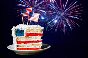 Good News on the Nation’s Birthday blog post by Ken Walker Writer. Pictured: An American flag colored cake, with American flags on top, and fireworks in the background.