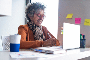 Pictured: An older woman sitting at a desk working on a laptop.