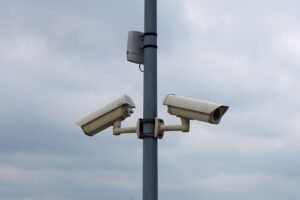 The Need to Turn Down the Thermostat blog post by Ken Walker Writer. Pictured: Two security cameras on a tall pole.