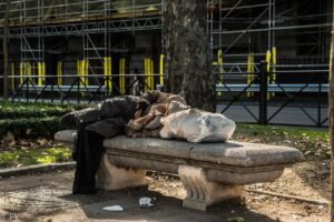 Pictured: A homeless man sleep on a concrete bench using a bag as a pillow.