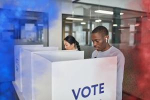 Election: Power of the People blog post by Ken Walker Writer. Pictured two people voting at the polls on the left is a blue wave of smoke, on the right a red column of smoke.